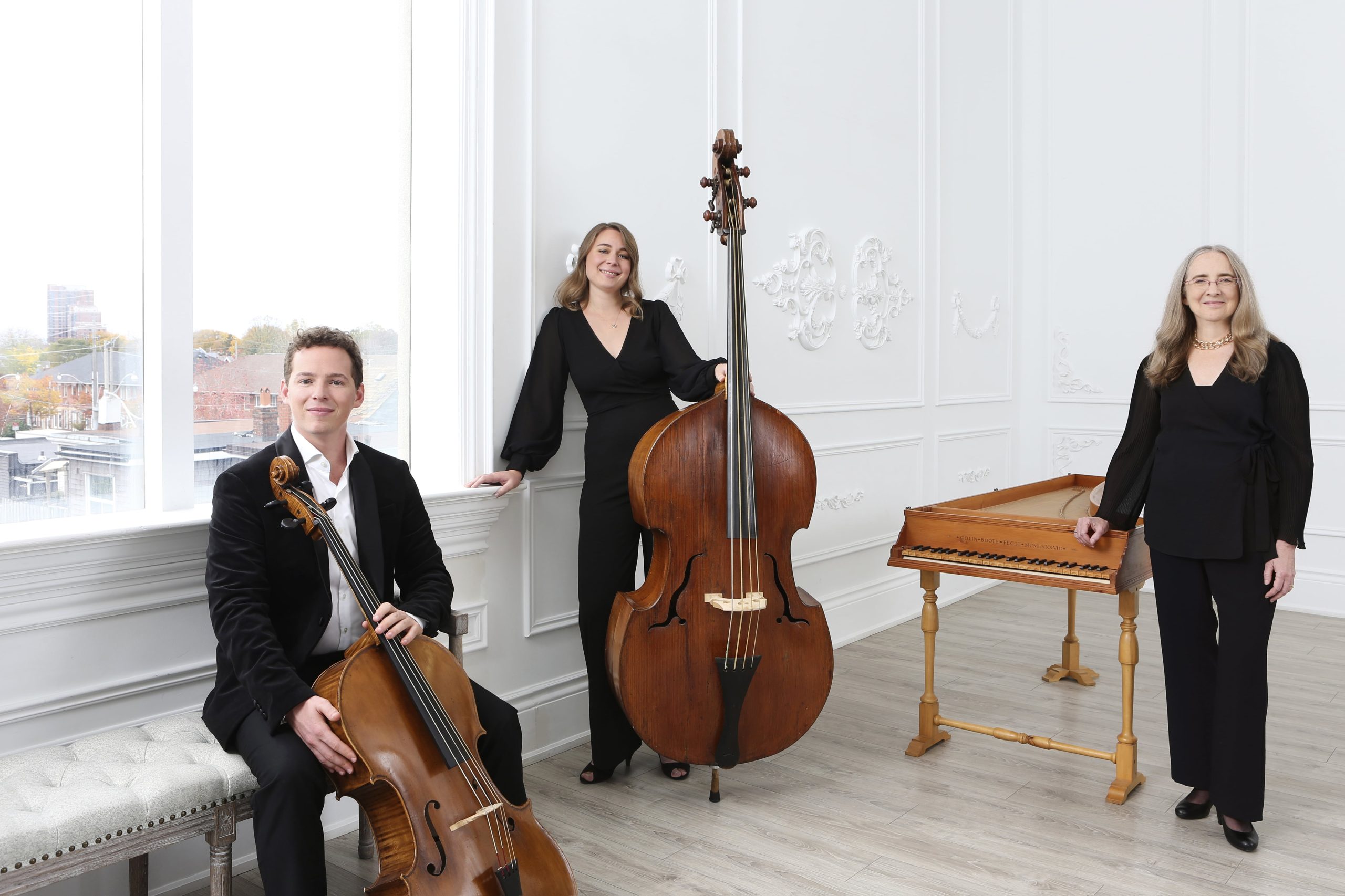 Three musicians standing holding instruments, cello, harpsichord