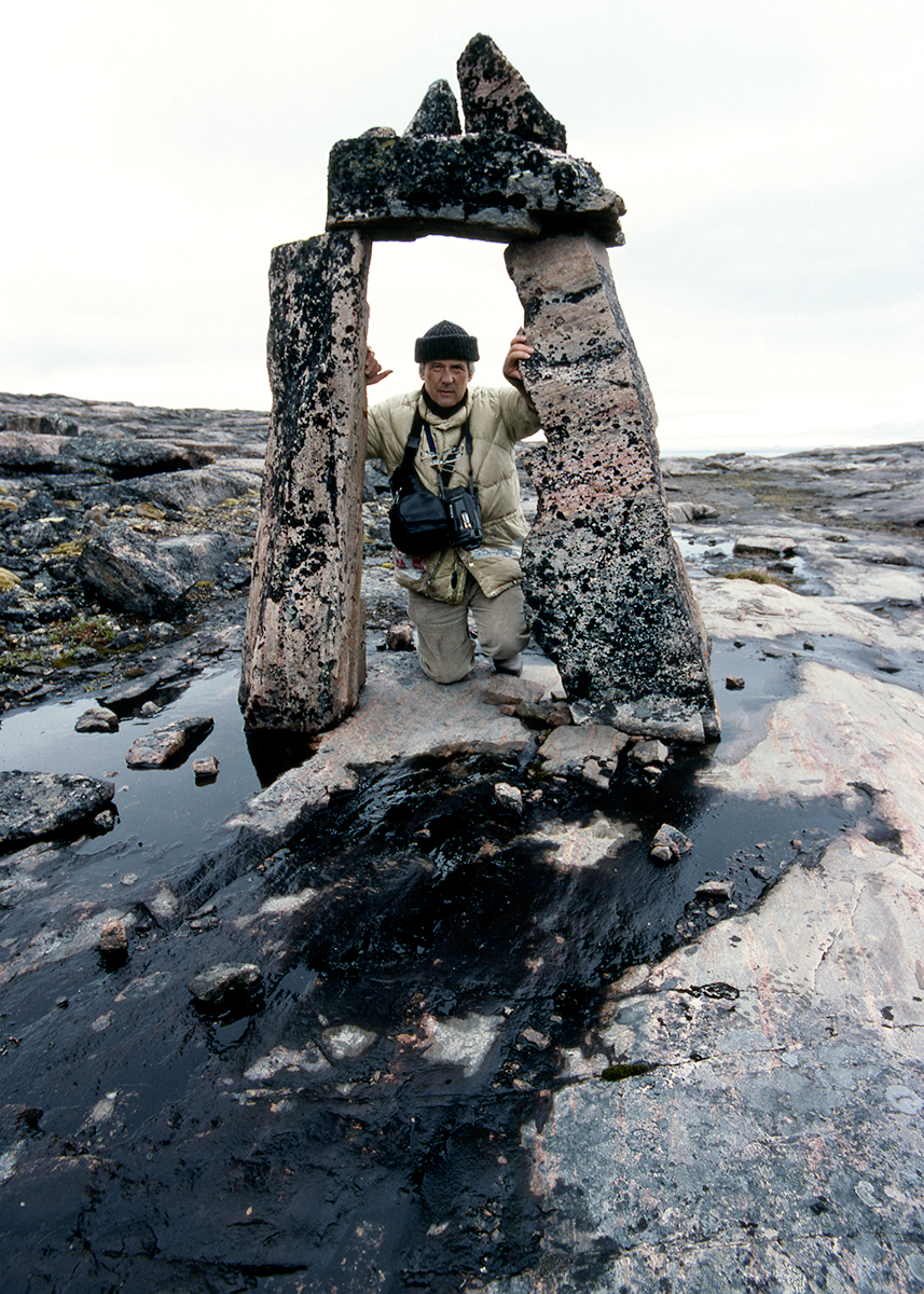 Norman Hallendy photo of man kneeling in stone archway in rocky landcsape