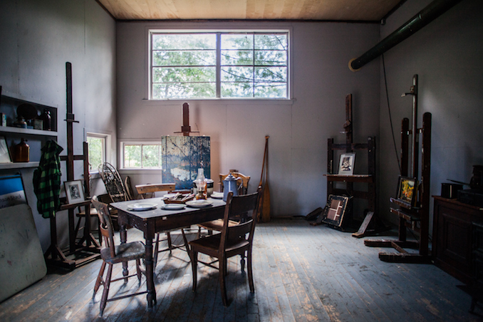 Tom Thomson shack photograph of the interior of a room with window; table, chairs and artwork on easels